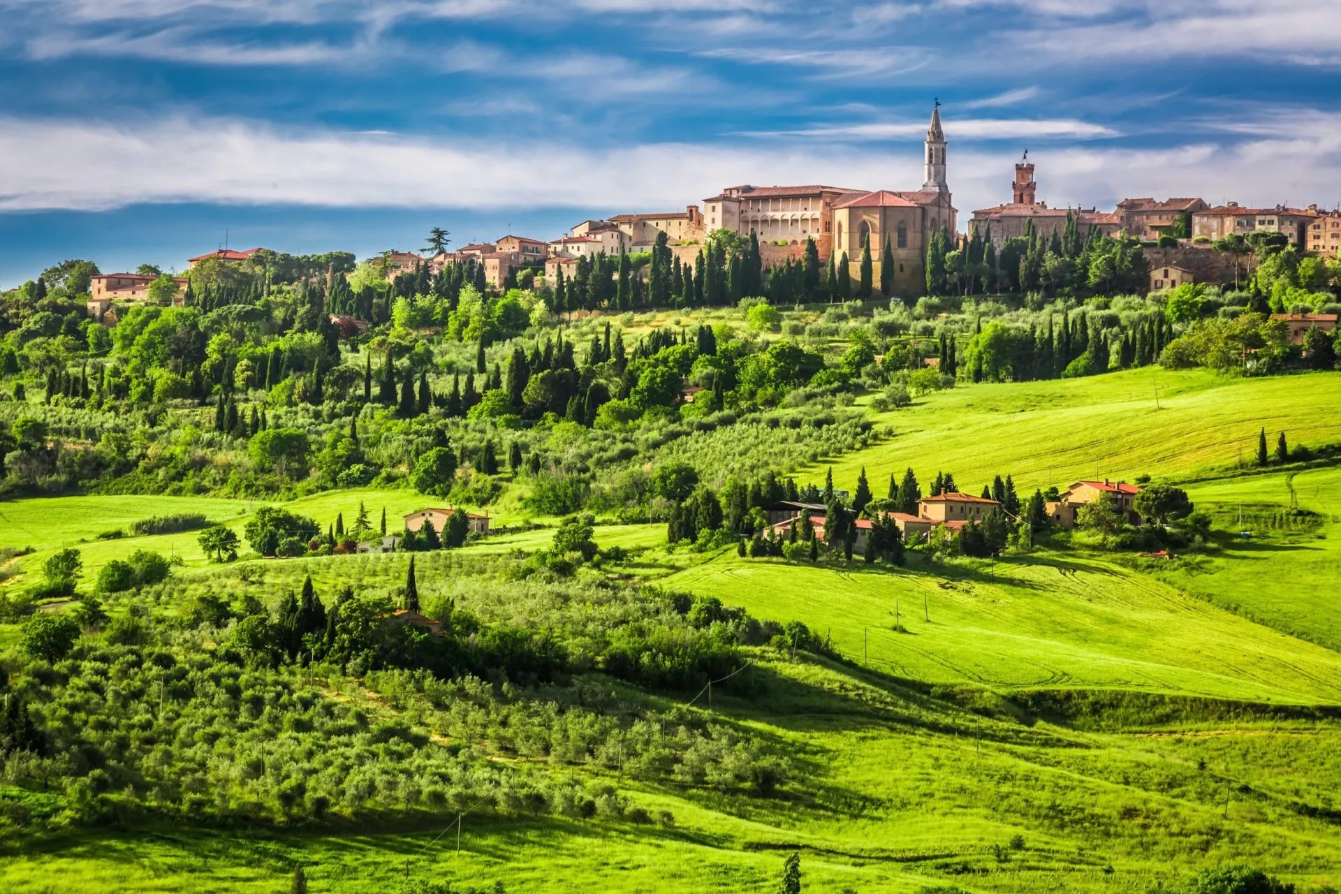 Hilltop town of Pienza with historic buildings surrounded by vibrant green Tuscan countryside.