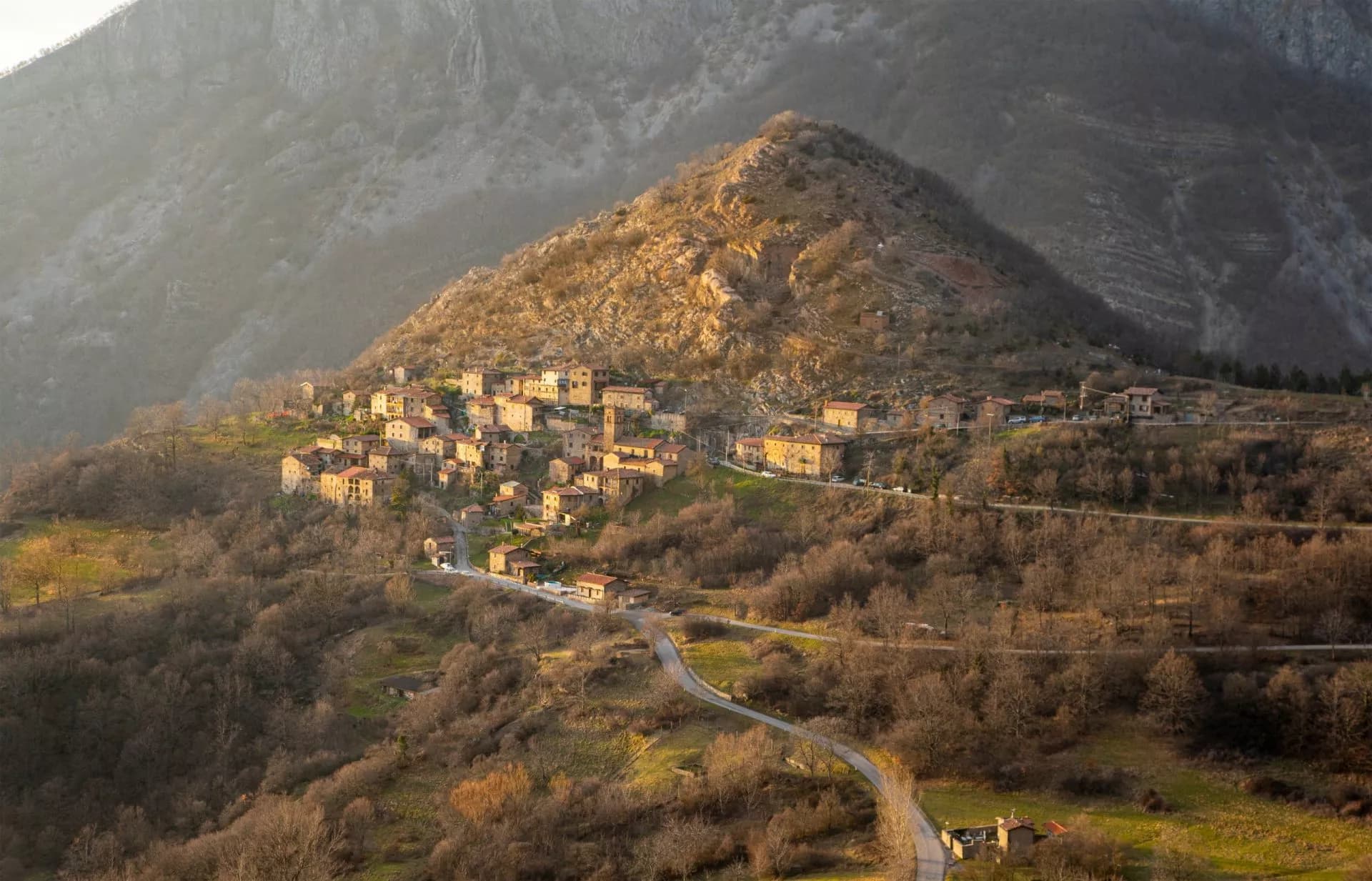 Hillside village of stone houses nestled on a slope under large mountains, Pania di Corfino.
