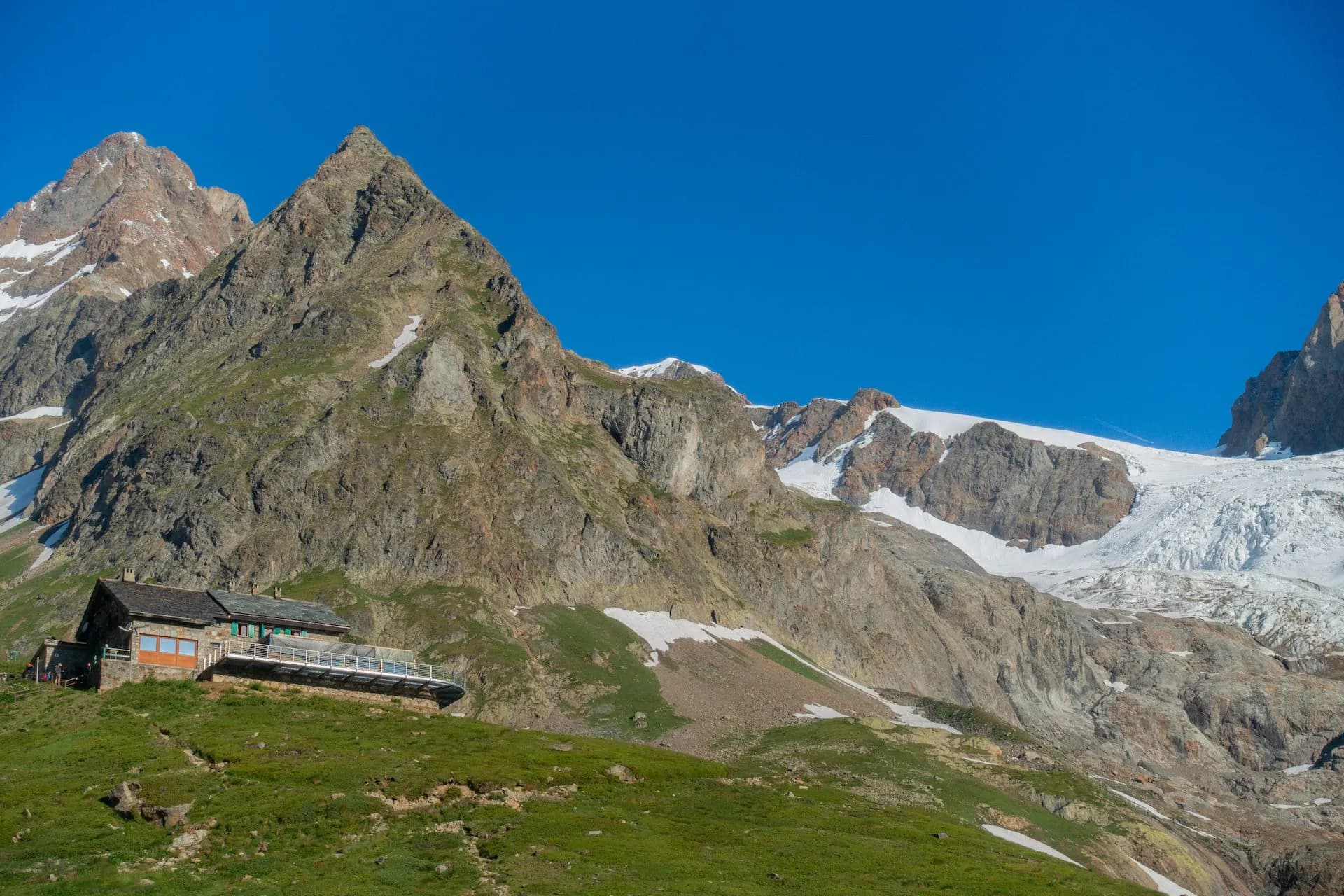 Rifugio Elisabetta Soldina below Glacier de la Lex Blanche, alpine hut on grassy slope.