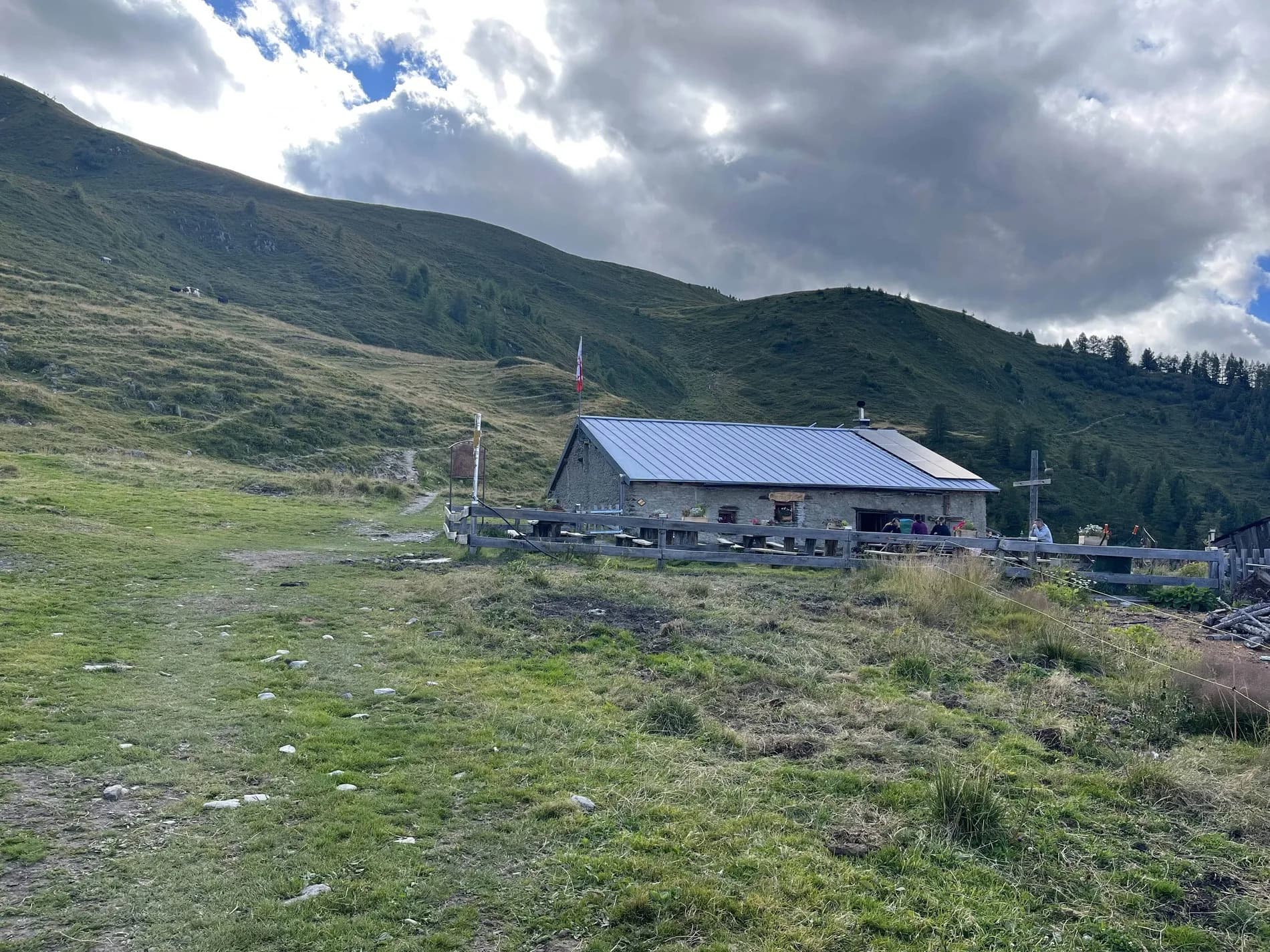 Stone mountain refuge with blue roof on grassy slope under cloudy sky, near Alpage de Bovine.