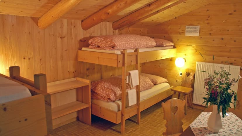 Wooden bunk beds in an attic room with log beams, illuminated by a wall lamp, Rifugio Scotoni.