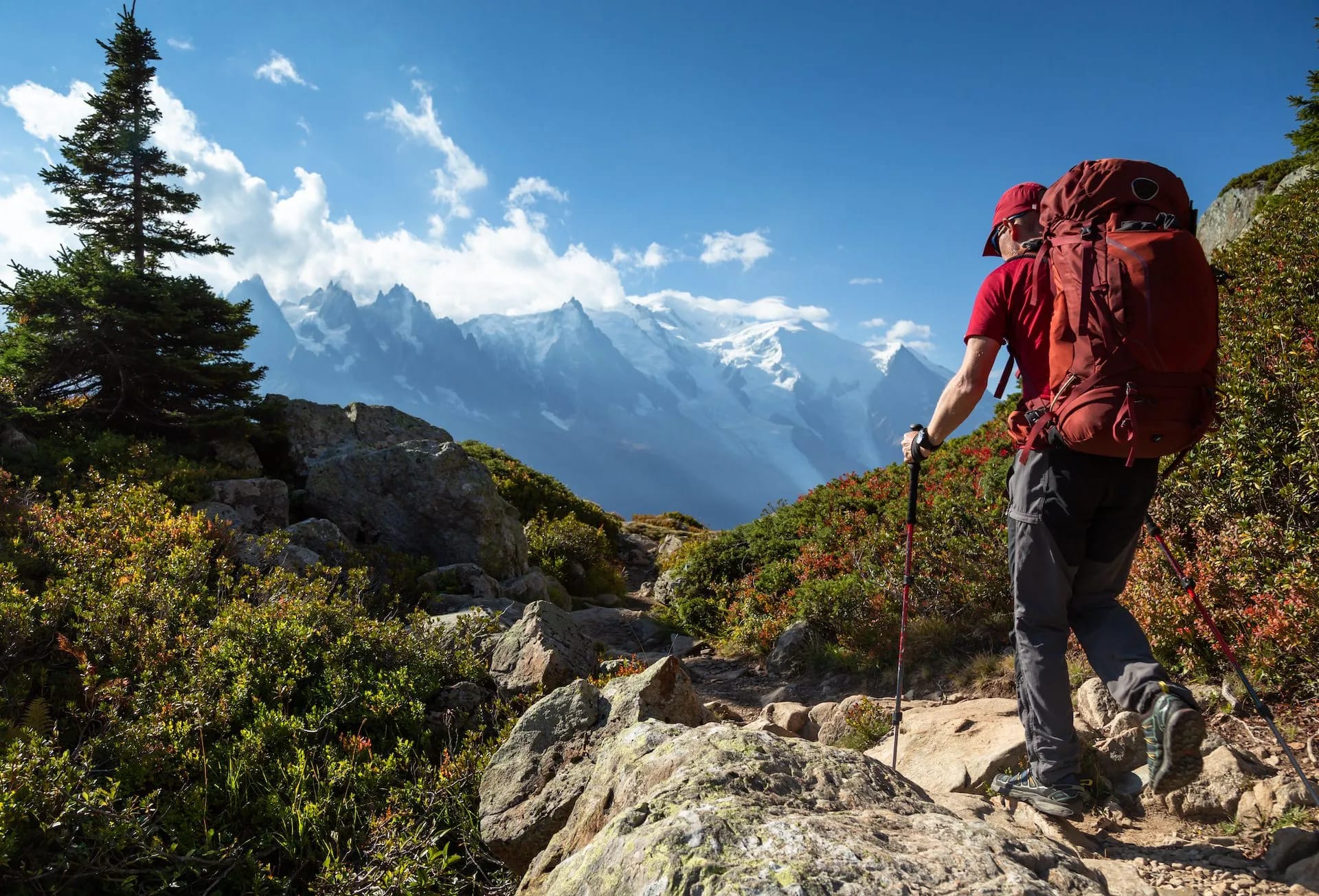 Hiker with large backpack trekking on rocky trail toward snow-capped mountains near Chamonix.