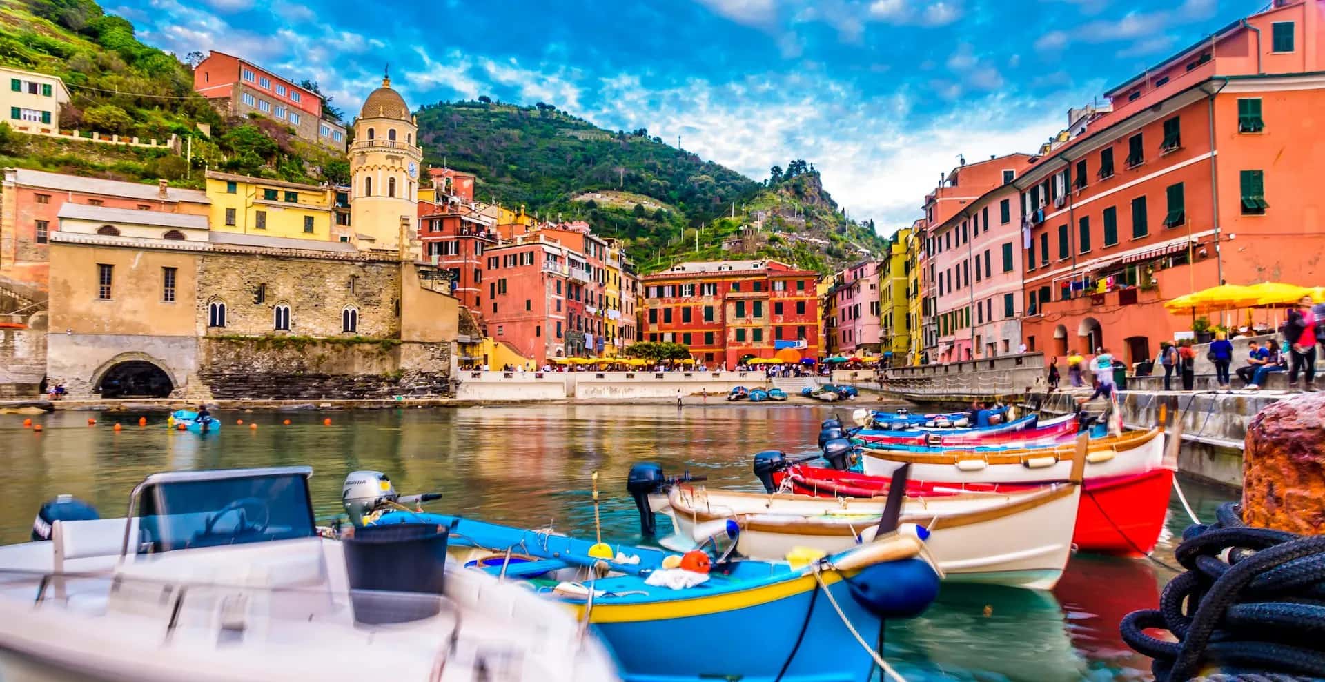 Colorful boats moored in harbor with colorful buildings and steep green hills of Vernazza.