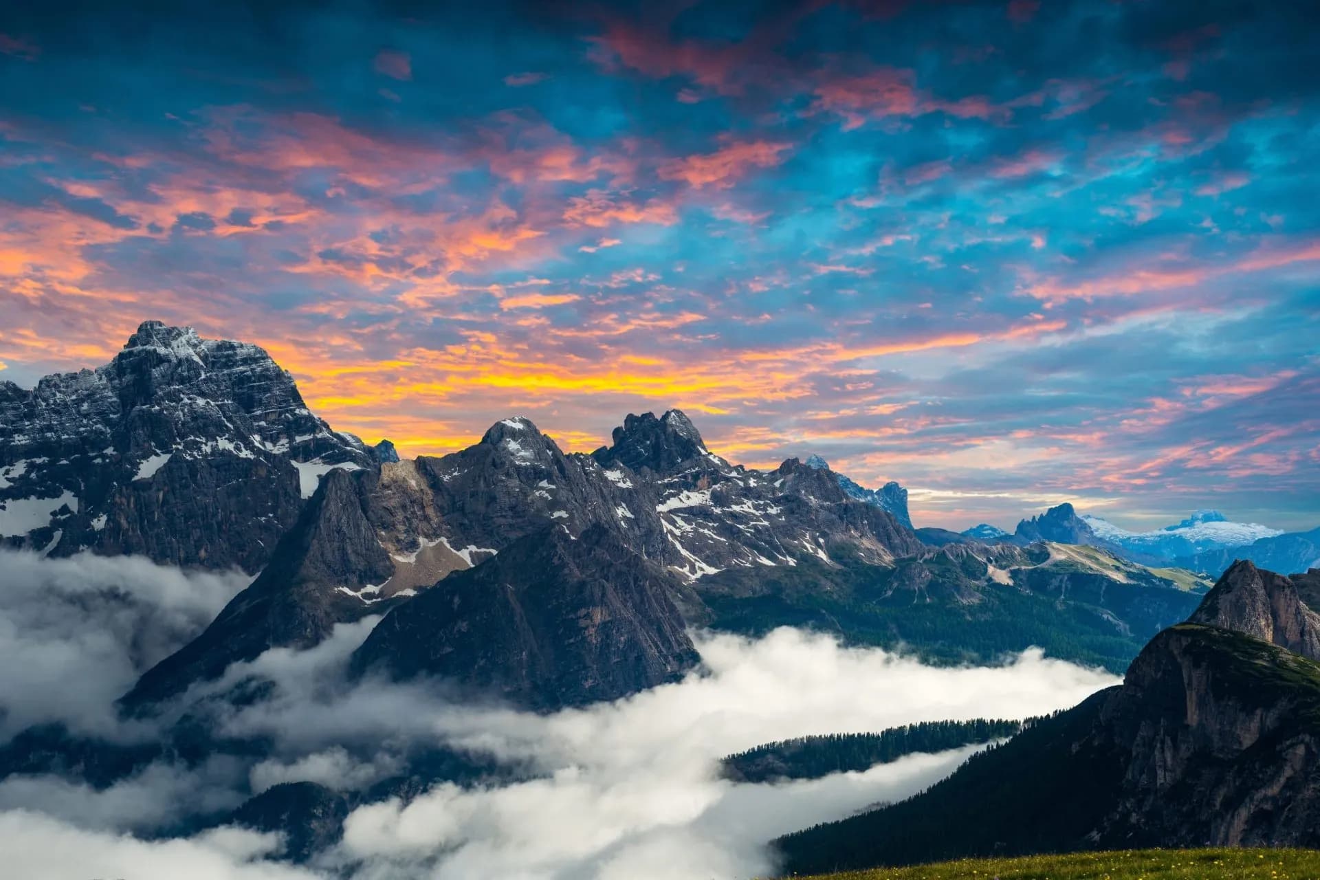 Dolomites mountains with snow patches above clouds at sunrise with pink and blue sky