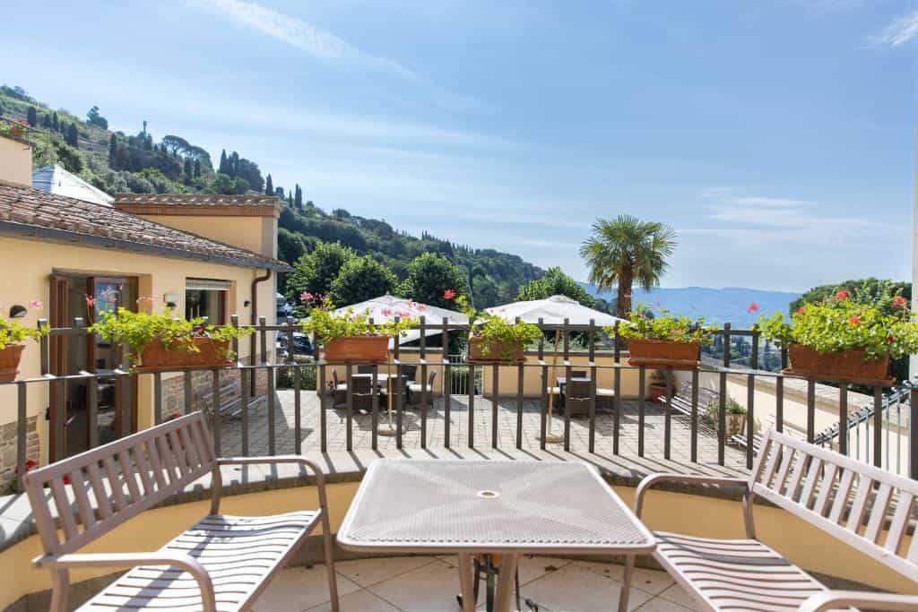 Terrace with metal furniture overlooking lush green hills and distant mountains under blue sky.