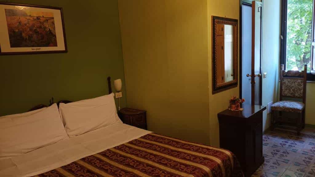 Bedroom with green walls, a made bed with white linens, and a wooden chair near a window.