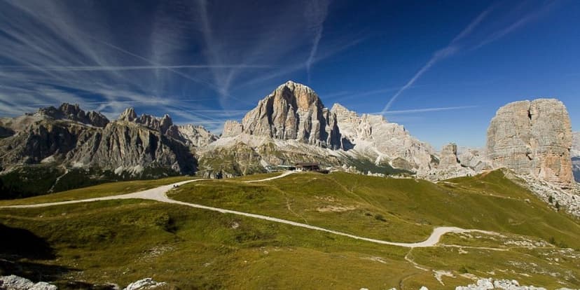 Mountain landscape with Rifugio Scoiattoli, hiking path, and dramatic peaks under a blue sky.