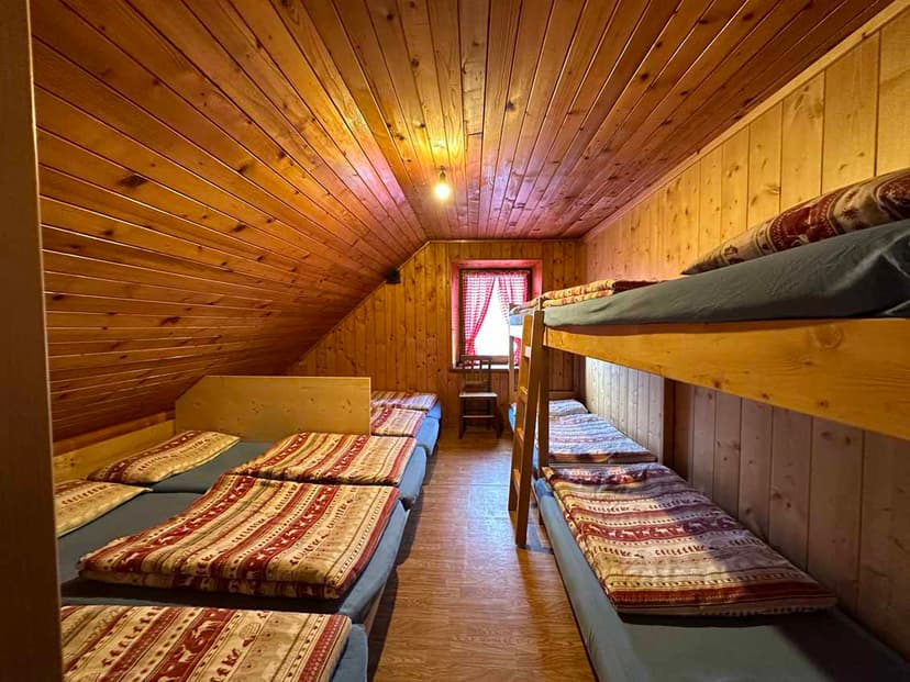 Dormitory room with wooden walls, bunk beds, and single beds with patterned blankets at Rifugio Adolfo Sonino al Coldai.