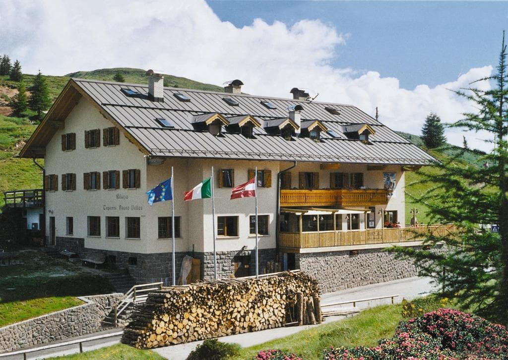 Alpine lodge with wooden balconies and flags in a mountain landscape.