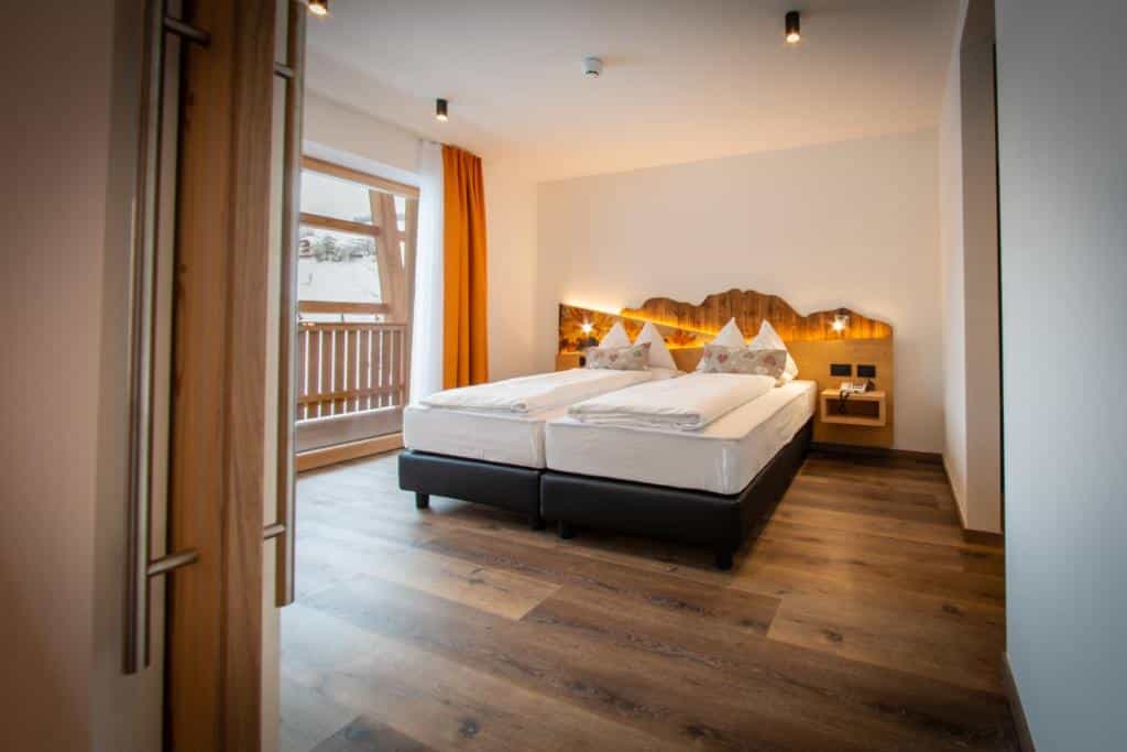 Modern hotel bedroom interior with twin beds, wooden floor, and balcony door view of snow