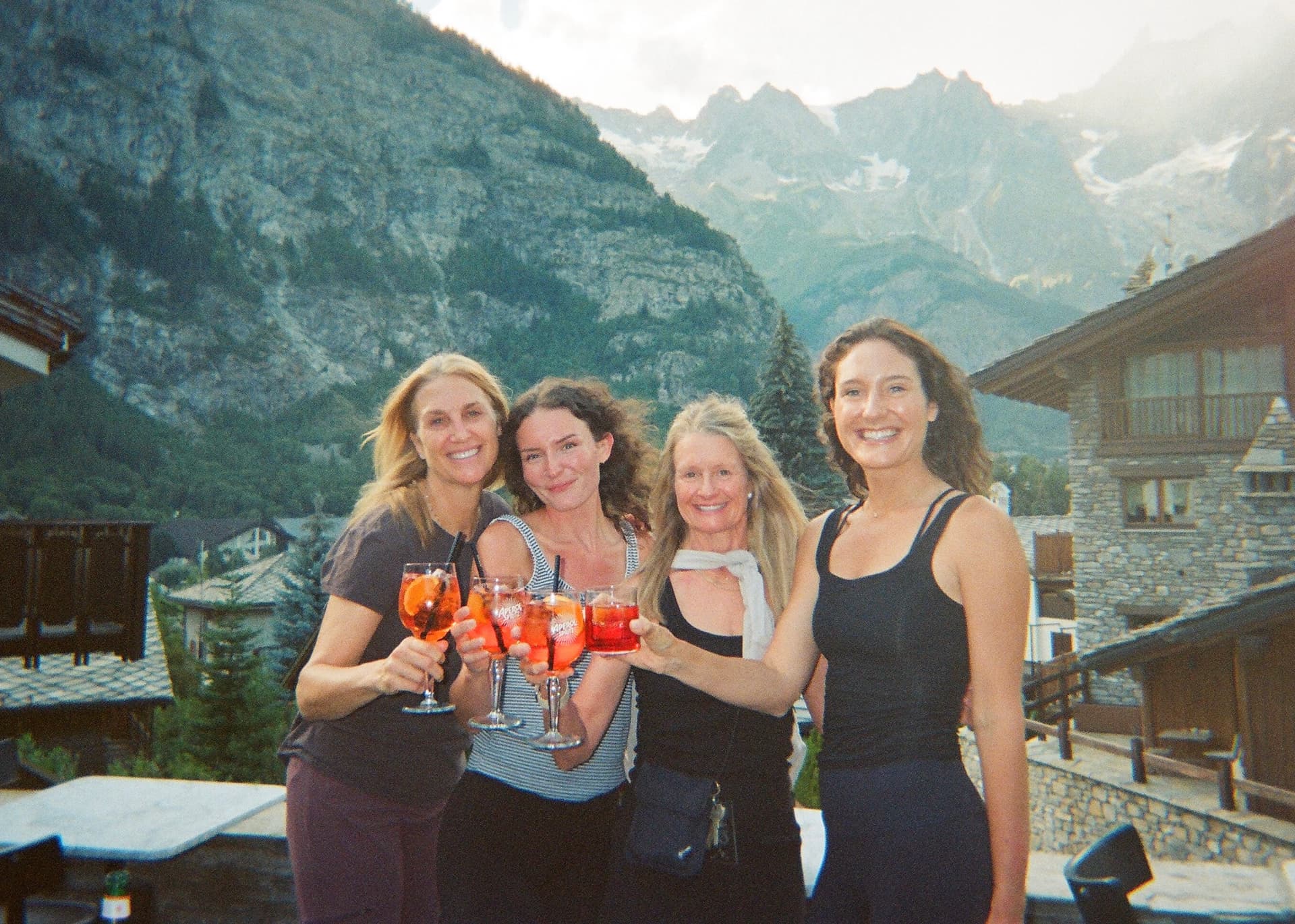 Friends toasting with drinks at an alpine mountain village with snow-capped peaks
