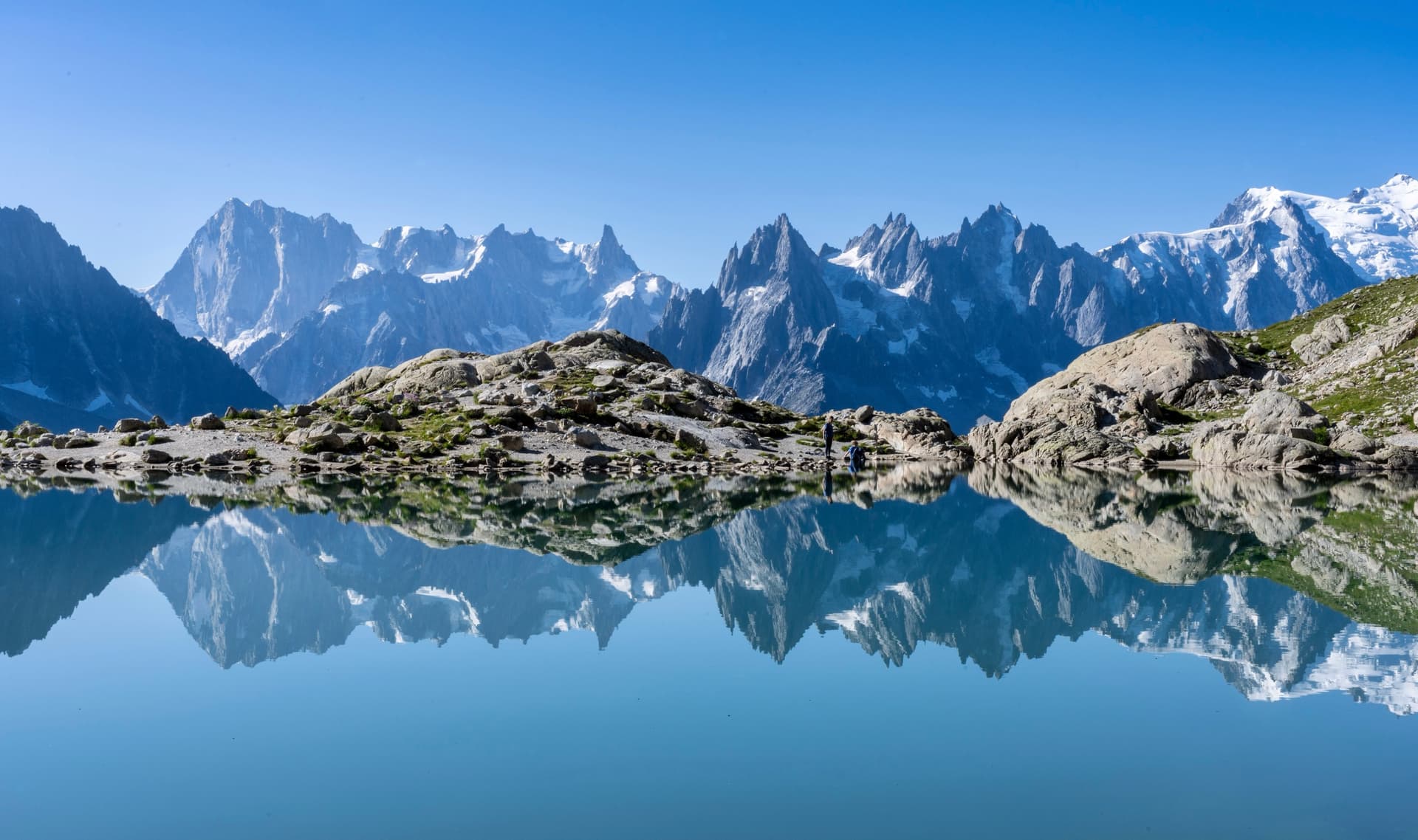 Alpine lake reflecting snow-capped mountain peaks and rocky shoreline