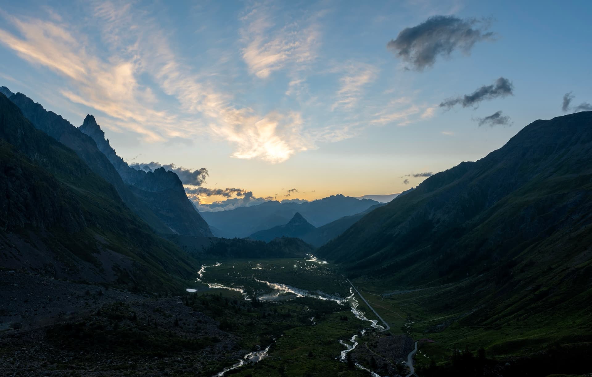 Alpine valley with winding river at sunset between mountain ridges
