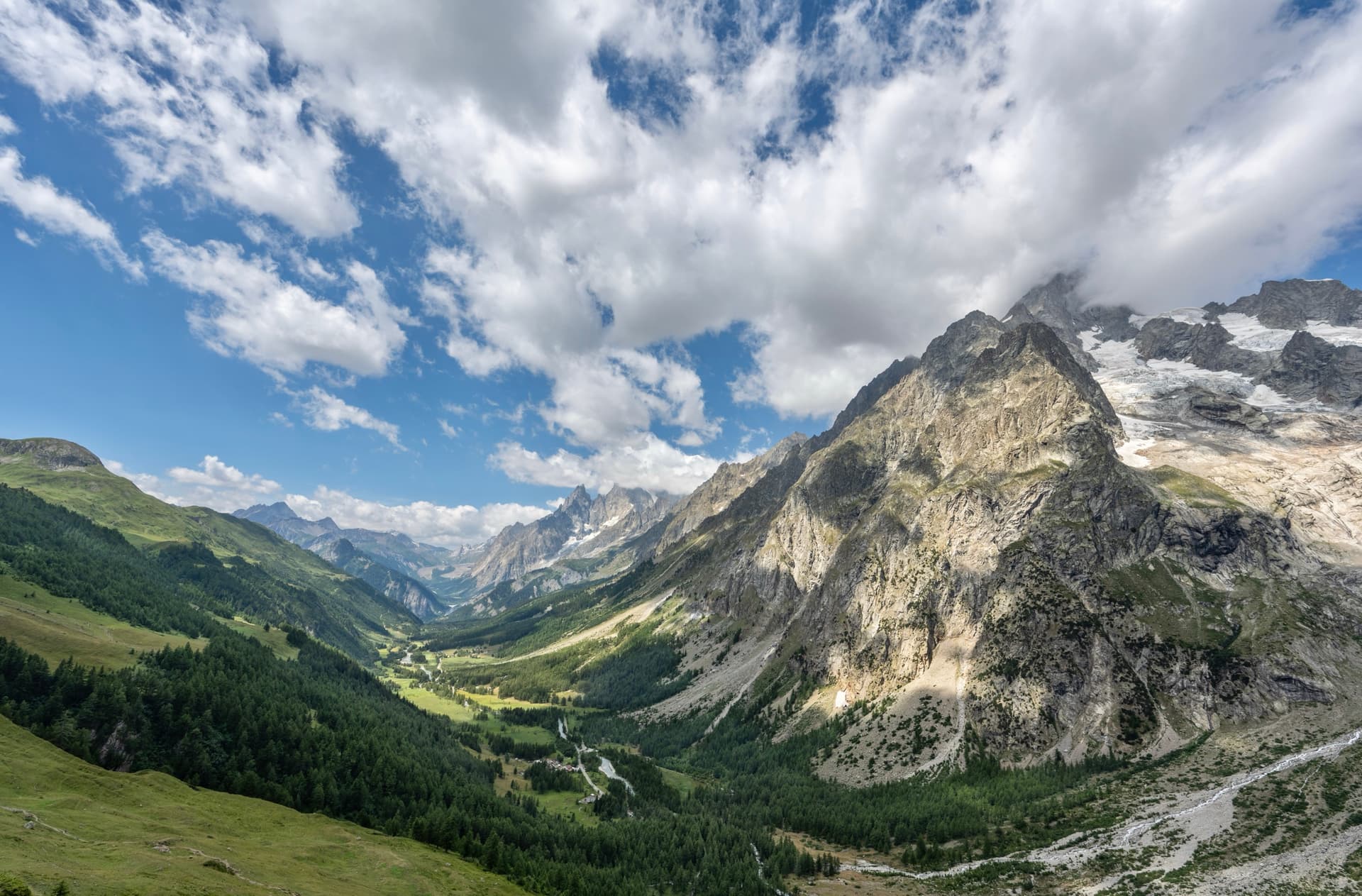Green valley under rocky mountain peaks with pine forest and cloudy sky