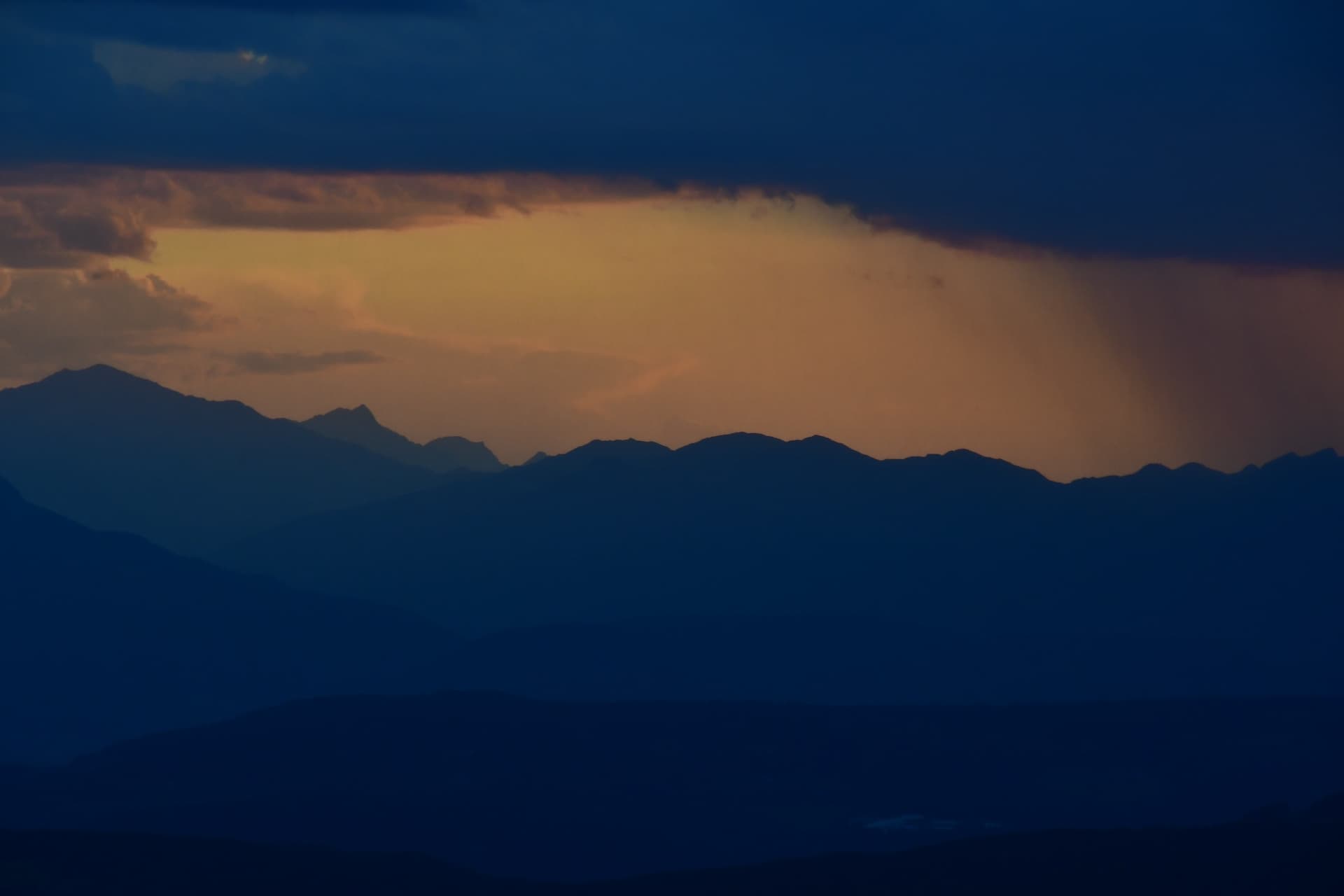 Mountain ridges silhouetted under dramatic storm light and sunset sky