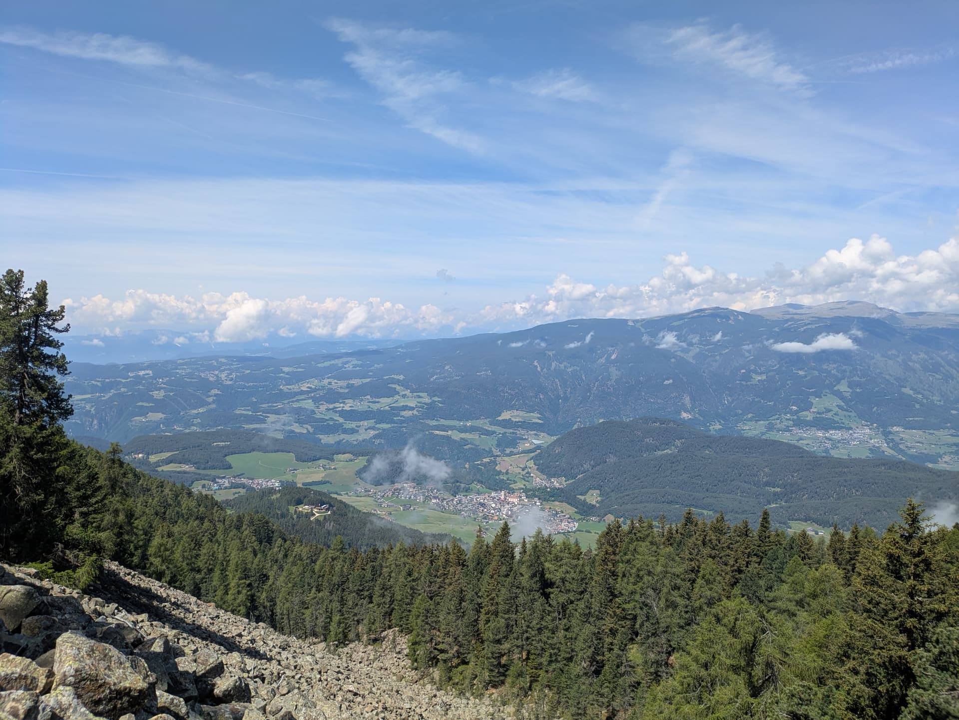 High-altitude view over wooded valleys with distant mountain ranges and scattered clouds in blue sky