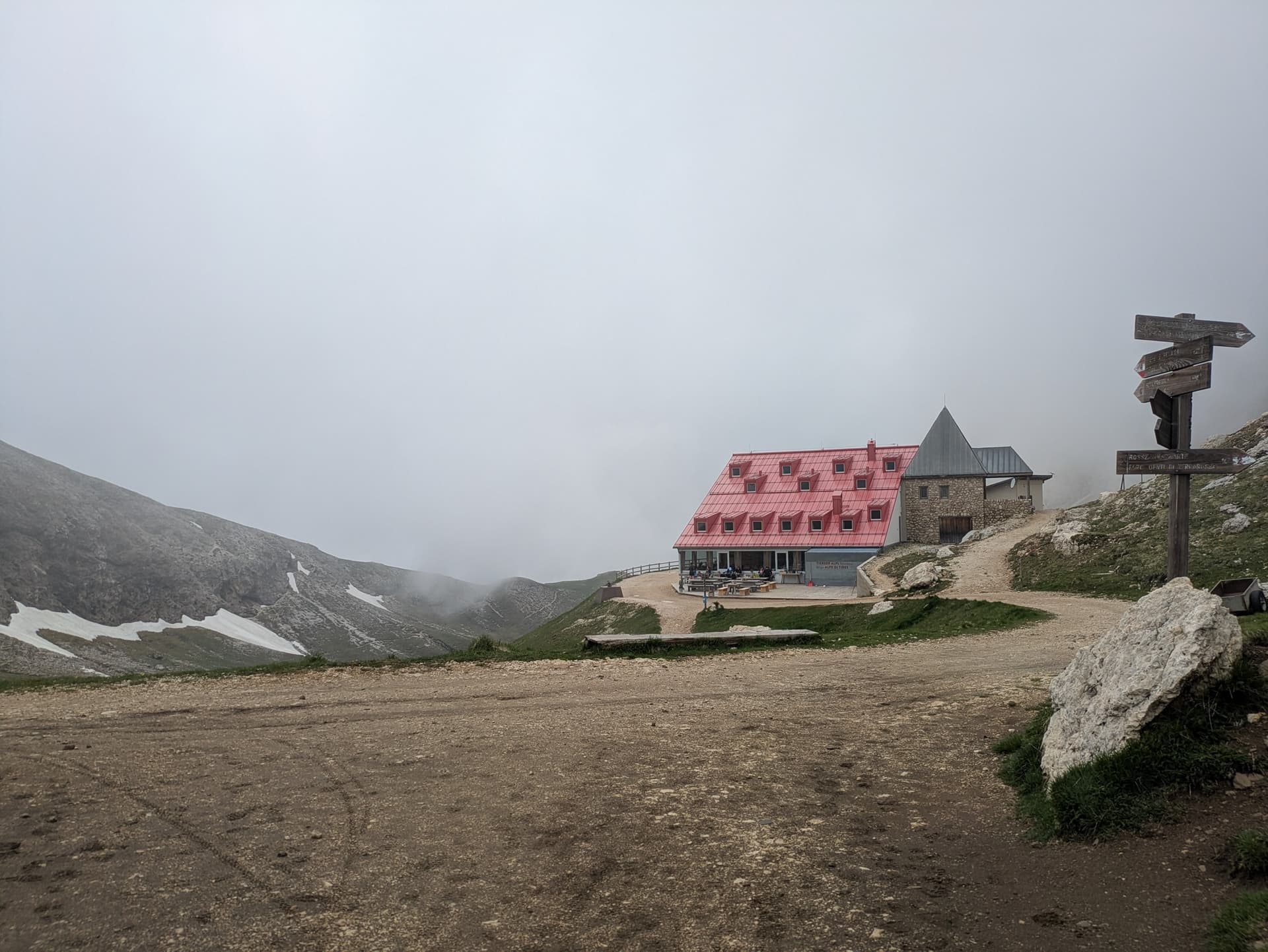 Red-roofed alpine hut and wooden signpost on foggy mountain trail