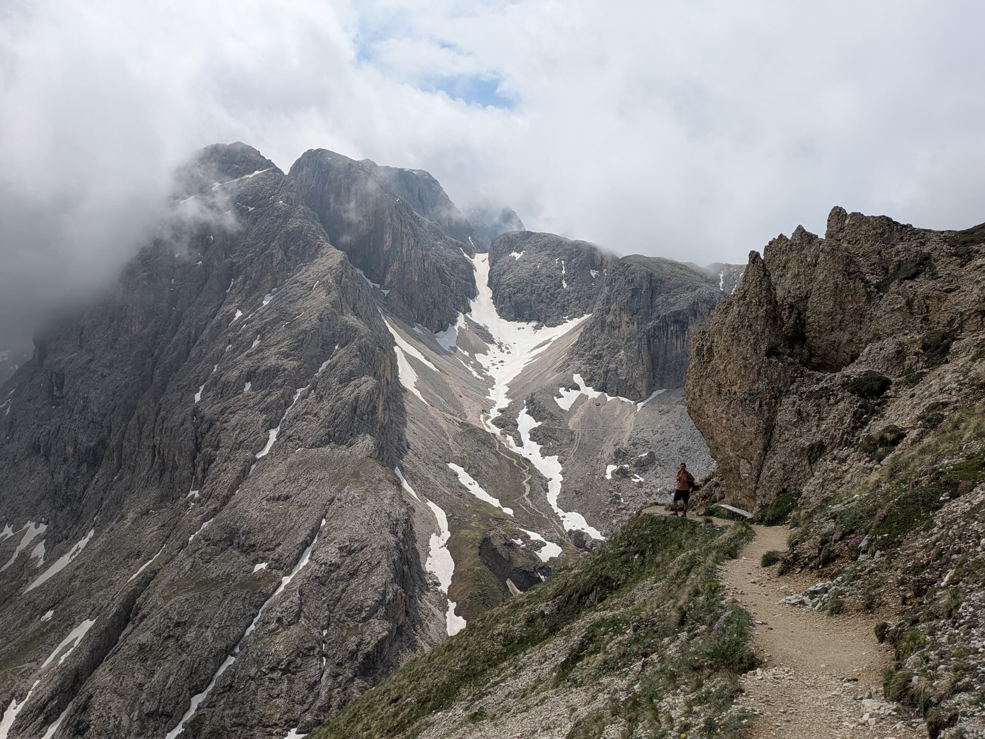 Hiker on rocky mountain trail with snow patches and cloudy peaks