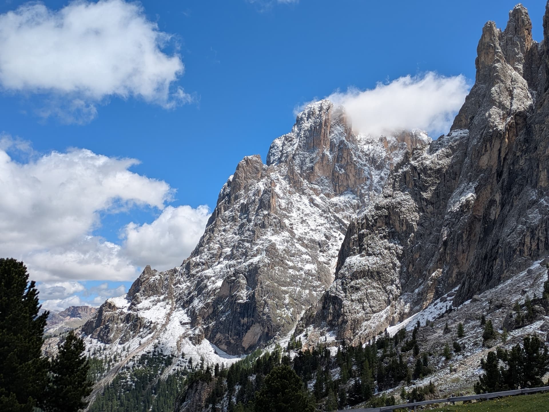 Jagged alpine mountain peaks covered with fresh snow and pine forest under a blue sky